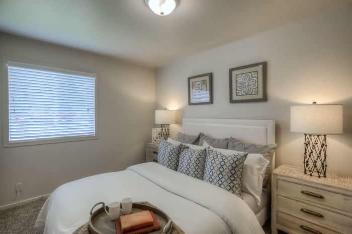 A master bedroom with a plush white headboard, decorative throw pillows, modern lamps, and soft natural lighting at Viewcrest Village in Bremerton, WA.