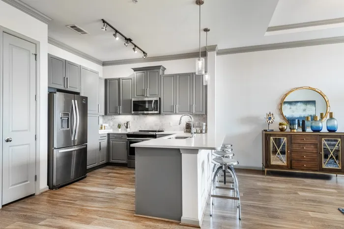 Modern kitchen with stainless steel appliances, sleek gray cabinets, and island seating at The Hendry in Garland, TX.
