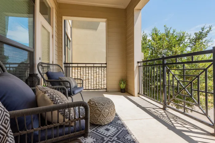 Private balcony with cozy seating and lush views at The Hendry Apartments in Garland, TX.