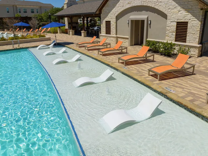 Resort-style swimming pool with modern in-water loungers and vibrant orange umbrellas at The Hendry in Garland, TX.