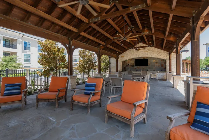 Outdoor fireplace lounge area with plush orange seating and pool views at The Hendry in Garland, TX.