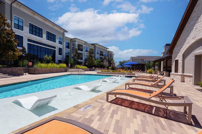 Resort-style swimming pool with modern in-water loungers and vibrant orange umbrellas at The Hendry in Garland, TX.