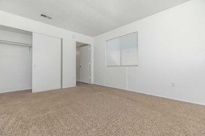 Light-filled bedroom featuring soft carpet flooring, white walls, and spacious closet storage at Lifestyles at Renaissance Apartments in Albuquerque, NM.