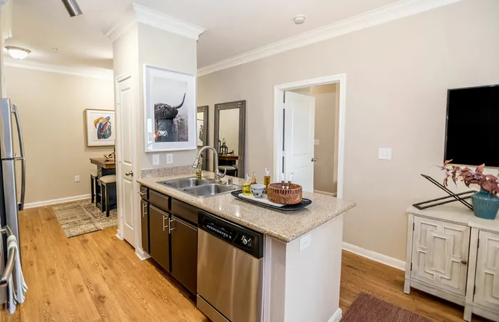 a room filled with natural light showcasing a beautiful kitchen bar with black cabinets and a stainless steel dishwasher, all surrounded by impressive hardwood floors