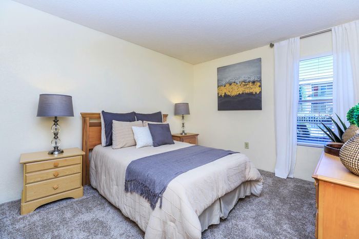 a large room filled with a warmly-dressed bed, two nightstands, and a large window allowing for plenty of natural light