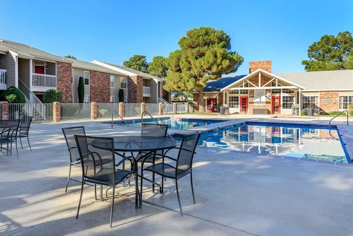 Sparkling poolside area with outdoor seating at Whispering Pines Apartments, ideal for relaxation in El Paso, TX.