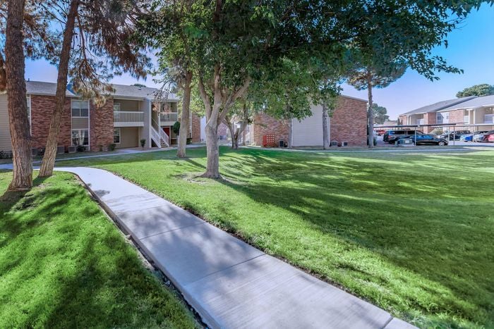 Whispering Pines Apartments' open grassy spaces with walking paths, surrounded by beautiful trees in El Paso, TX.