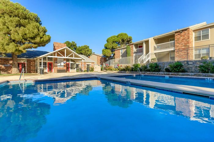 Large pool surrounded by mature trees and peaceful landscaping at Whispering Pines Apartments in El Paso, TX.