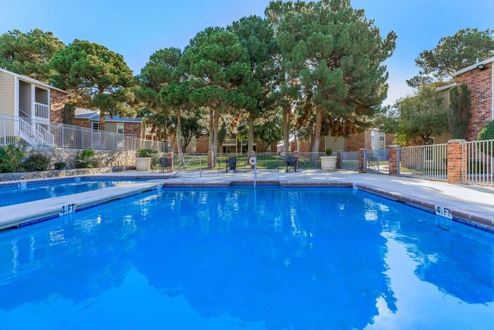 Crystal-clear pool surrounded by well-maintained landscaping at Whispering Pines Apartments in El Paso, TX.