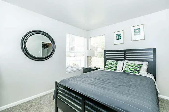 a large bedroom with a cozy bed and two windows letting in a lot of natural light