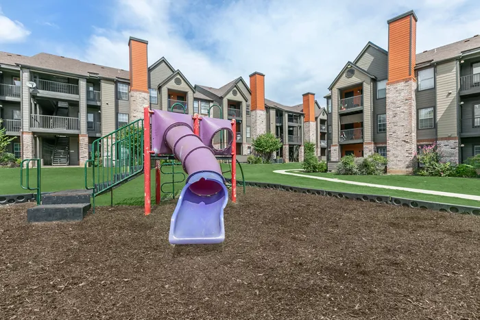 an outdoor playground equipped with stairs, a slide, and some climbing equipment - atop a large open surface of woodchips