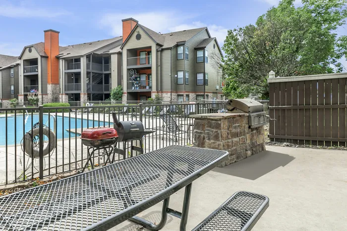 a picnic table, grills, and a smoker overlooking a swimming pool