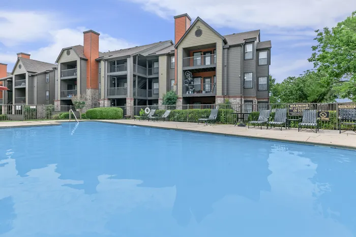 an apartment building overlooking a large clean swimming pool with loungers and tables along the edge