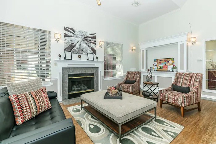 a large room that resembles a living room, complete with a fireplace, couch, chairs, padded table, and some other decor - all basking in natural light