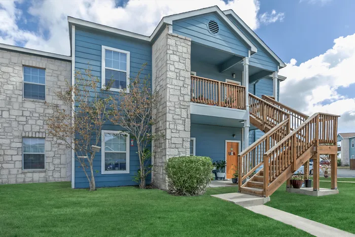 Modern apartment building with stone accents, wooden stairs, and landscaping at Portside Villas in Ingleside, TX