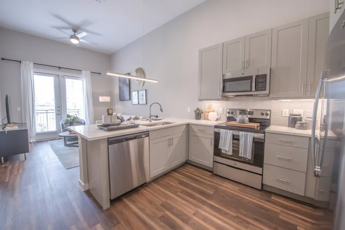 modern kitchen with hardwood floors, stainless steel appliances, white cabinets and countertop, and natural light flooding from a large window.