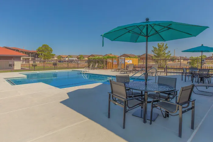 Outdoor pool area with umbrellas, tables, and loungers at Santa Teresa Terrace in Santa Teresa, NM.