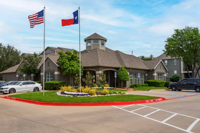 Welcoming entrance of Oak Park Apartments in Euless, TX, featuring colorful landscaping and U.S. and Texas flags.