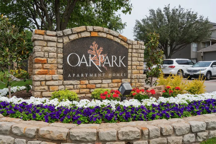 Beautifully designed property sign of Oak Park Apartments in Euless, TX, surrounded by colorful flowers and greenery.