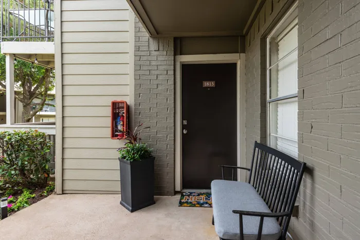 Welcoming apartment entrance at Oak Park Apartments in Euless, TX, with a cozy bench and vibrant potted plants.