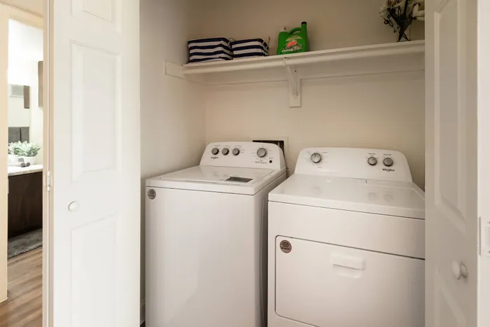 In-home laundry room at Oak Park Apartments in Euless, TX, with a washer, dryer, and convenient shelving.