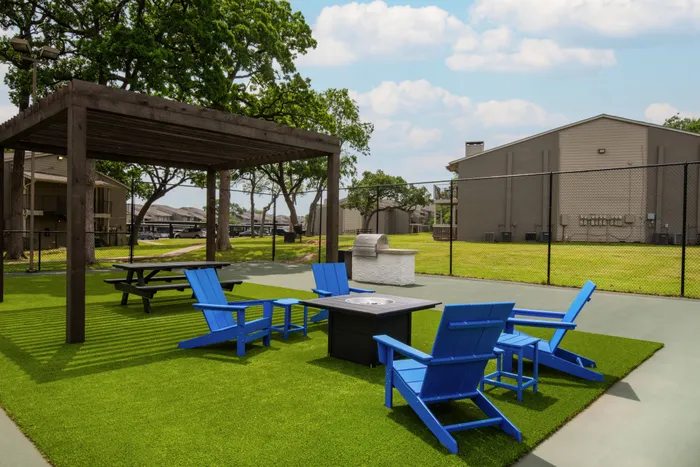 Relaxing outdoor lounge area at Oak Park Apartments in Euless, TX, with a pergola, Adirondack chairs, and a fire pit.