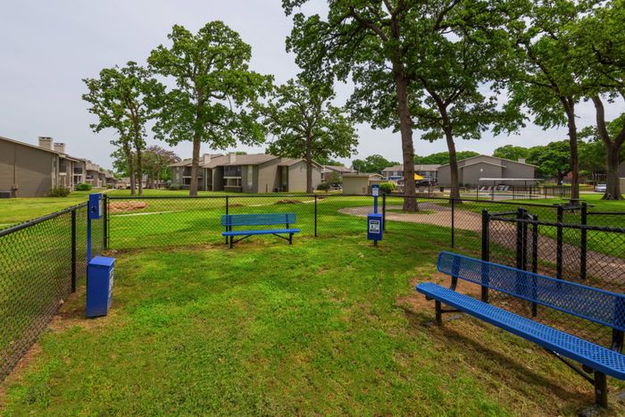 Spacious dog park at Oak Park Apartments in Euless, TX, with benches and open space for your furry friends to play.