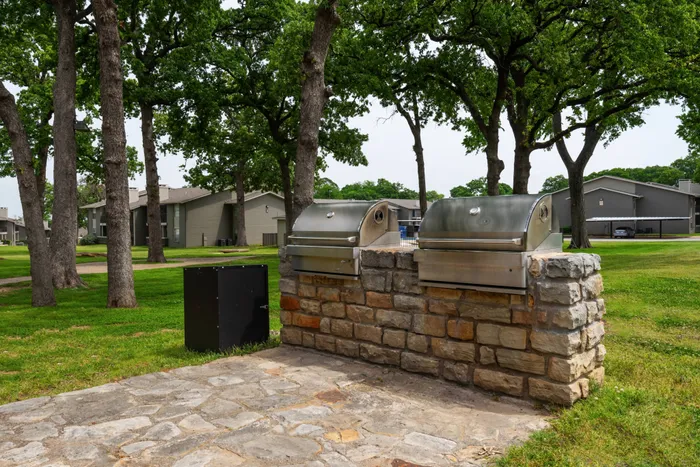 Outdoor grilling area at Oak Park Apartments in Euless, TX, featuring stone counters and stainless steel grills.