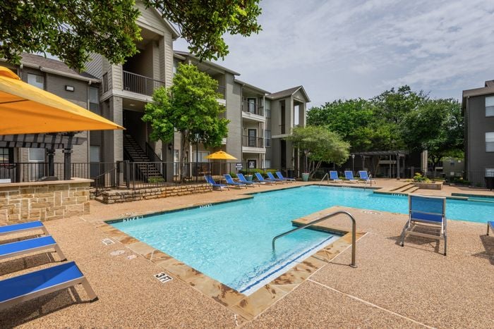 Resort-style swimming pool at Oak Park Apartments in Euless, TX, surrounded by lounge chairs and vibrant landscaping.