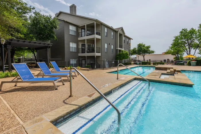 Resort-style swimming pool at Oak Park Apartments in Euless, TX, surrounded by lounge chairs and vibrant landscaping.