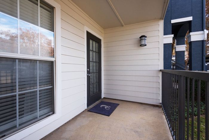 Outdoor patio with metal railing, black door, and a doormat