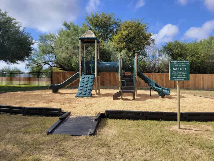 a playground with two slides, a tunnel, and some climbing equipment, all atop a woodchip-covered surface