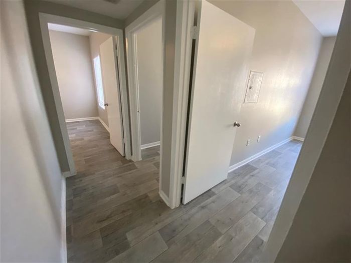 a hallway connecting three bedrooms, each with hardwood vinyl flooring