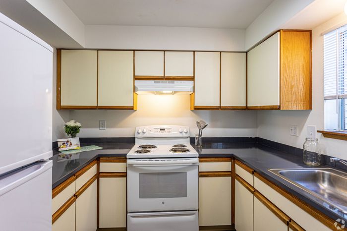 Bright and functional kitchen with wood and white cabinetry, electric stove, and sink at Winton Woods Apartments in Poulsbo, WA.