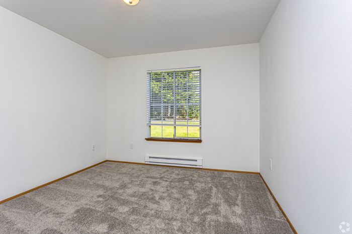 Well-lit bedroom with plush carpeting, a large window, and a clean design at Winton Woods Apartments in Poulsbo, WA.