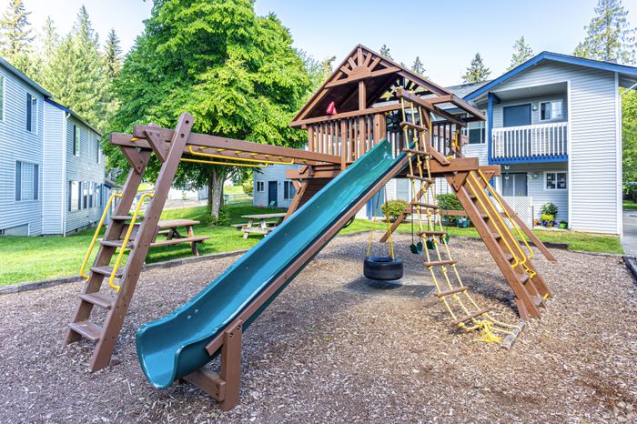 Outdoor playground with slides, climbing structures, and a safe play area at Winton Woods Apartments in Poulsbo, WA.