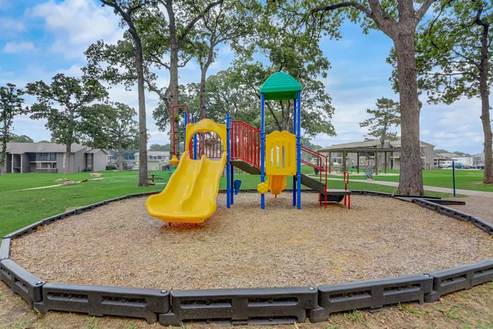 Colorful playground surrounded by lush greenery at Oak Park Apartments in Euless, TX.