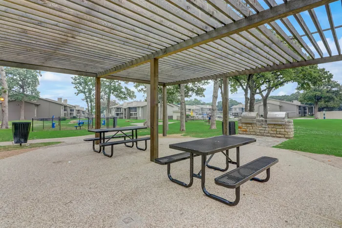 Shaded outdoor picnic area at Oak Park Apartments in Euless, TX, with picnic tables, grills, and a peaceful atmosphere.