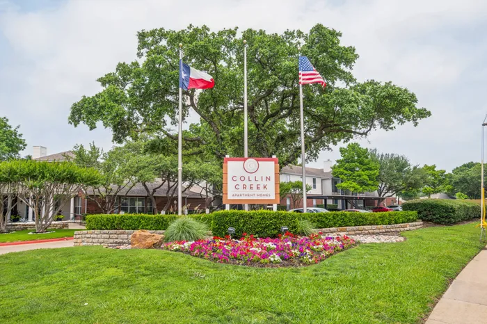 Beautiful entrance to Collin Creek Apartments with vibrant landscaping and flag displays in Plano, TX.
