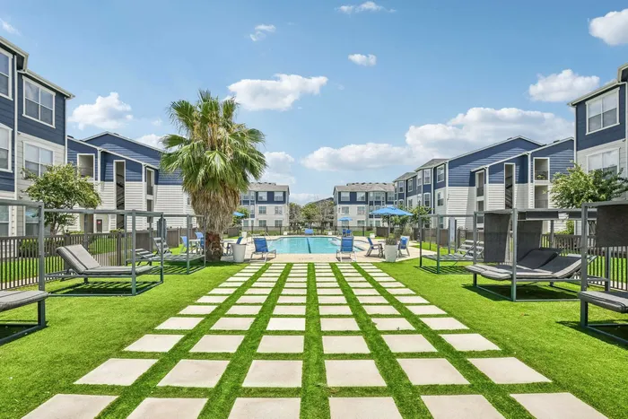 Outdoor swimming pool area with sleek loungers, palm trees, and a vibrant green lawn at Towne West Apartments, Houston, TX