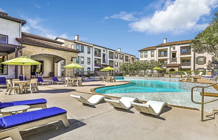 Outdoor pool area with white lounge chairs, Adirondack seating, and umbrellas at Amalfi at Tuscan Lakes in League City, TX.
