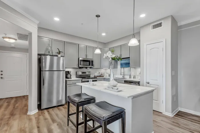 Modern kitchen with stainless steel appliances, pendant lighting, and dining area at Amalfi at Tuscan Lakes in League City, TX.
