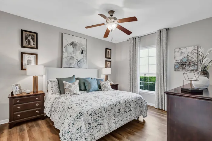 Elegant bedroom with modern décor, ceiling fan, and large windows at Amalfi at Tuscan Lakes in League City, TX.