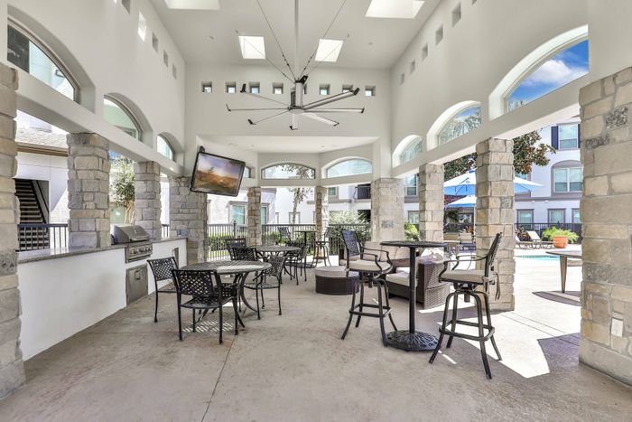 community outdoor grilling area with shaded patio seating, grills, flat-screen televisions, and a view of the swimming pool