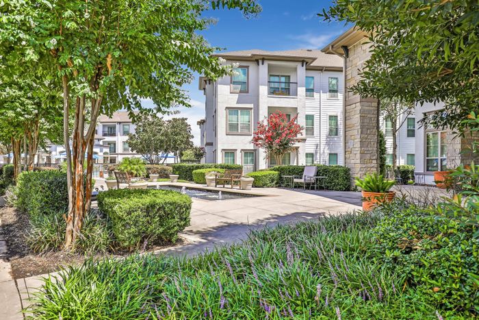 view of community with large apartment building, clean pathways, and professional landscaping