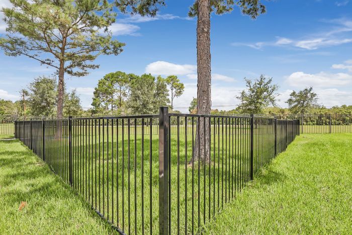 large metal fence surrounding green grass and filled with trees