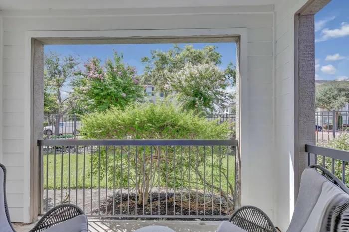 shaded patio with chairs and a metal railing overlooking greenery