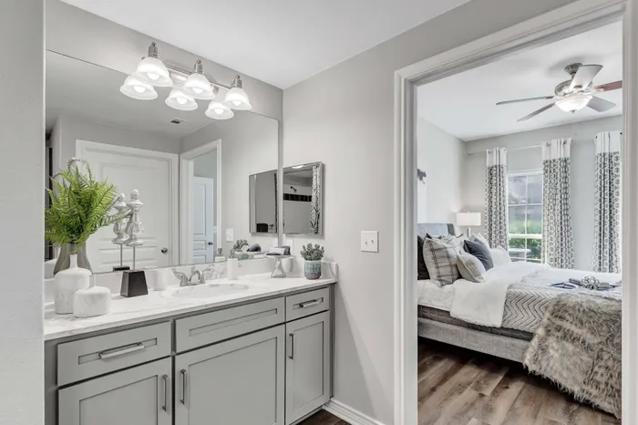 modern bathroom with light marble counter, gray cabinets, hardwood flooring, and a large mirror