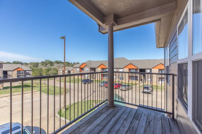 a wooden balcony with a metal rail overlooking the parking lot and other apartment buildings at Arbor Pines Apartments