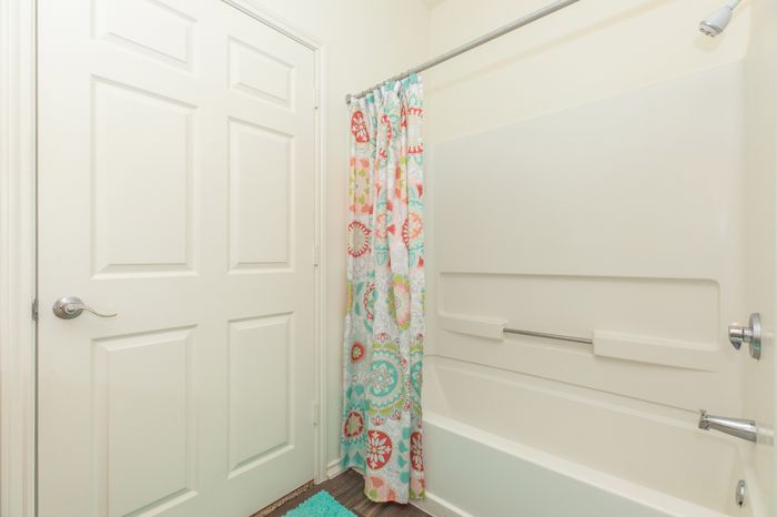 a clean bathroom with a white door, hardwood flooring, and a white bathtub